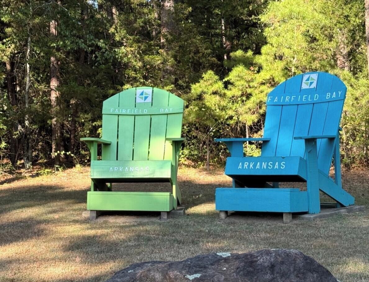 Two Adirondack chairs labeled 'Fairfield Bay' and 'Arkansas' in a wooded area.