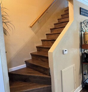 A wooden staircase with a handrail, a wall-mounted thermostat, and a decorative sign.