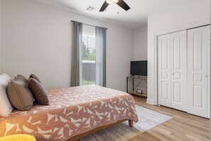 Ein Schlafzimmer mit einem Bett, einem Fernseher auf einem Schrank, einer weißen Tür und einem Fenster mit Vorhängen.