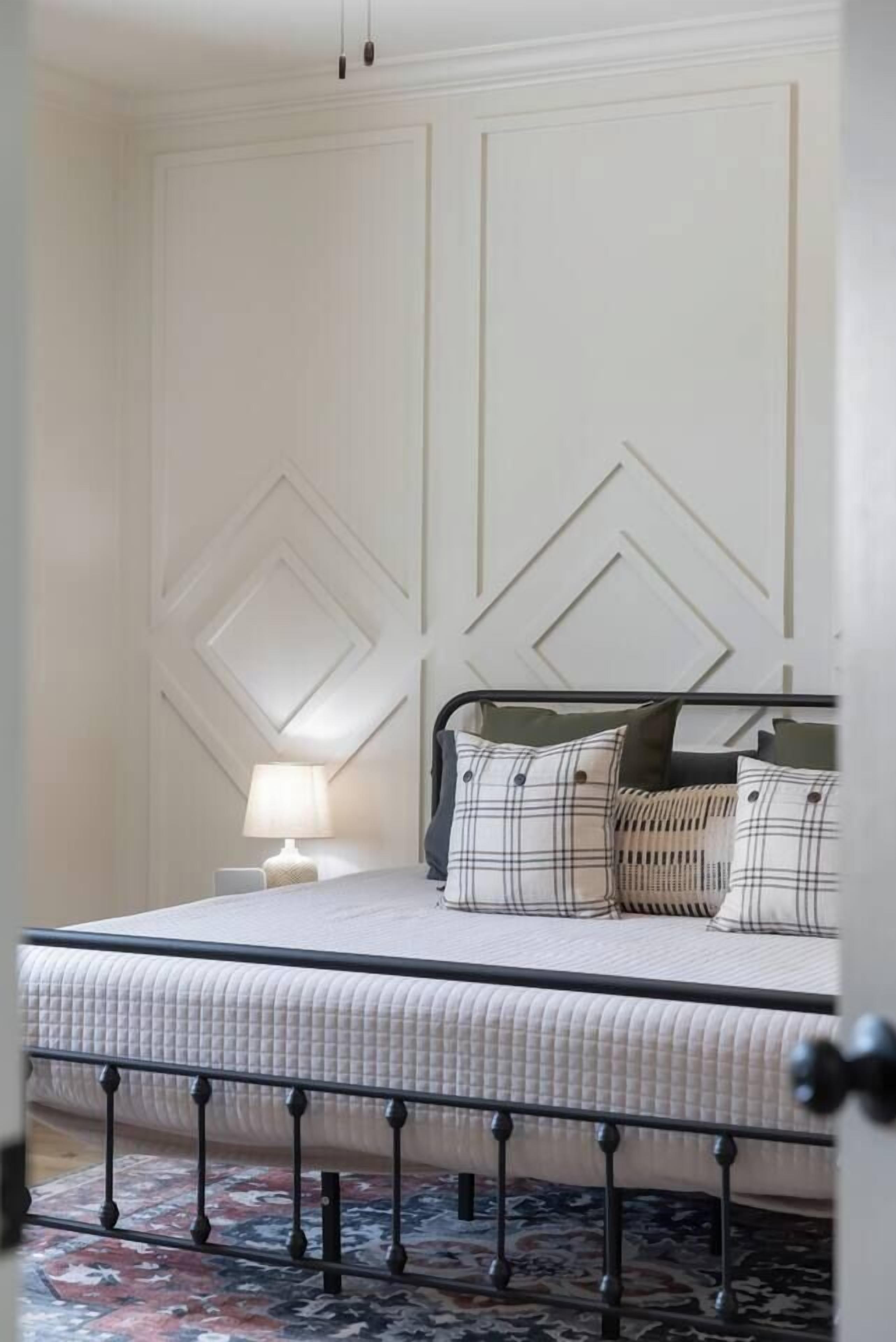A bed with a headboard, a bedside lamp, and a patterned rug.