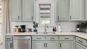 A kitchen with light green cabinets, a stainless steel dishwasher, a sink with a modern faucet, and various kitchen items on the countertop.
