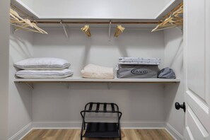 A closet with shelves holding pillows, a Graco mattress, and a black chair.