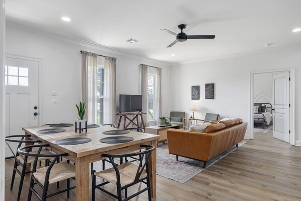 A modern living room with a sofa, a dining table with chairs, a television, and a ceiling fan.