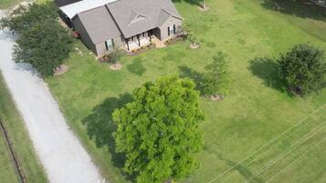 A residential property with a large lawn, a house with a sloped roof, and a prominent tree in the foreground.