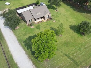 A residential property with a large lawn, a house with a sloped roof, and a prominent tree in the foreground.