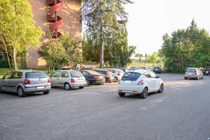A parking lot with several cars parked, surrounded by trees and a building with red brick walls. - Arma Doré Luxury Suite, Rome.  Free Pool & Parking! An elegant oasis of relaxation in Rome (Roma)