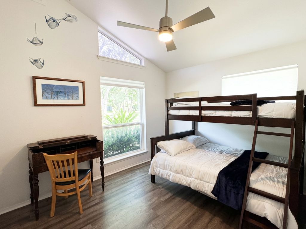 Una habitación con literas, un escritorio, una silla y un ventilador de techo.