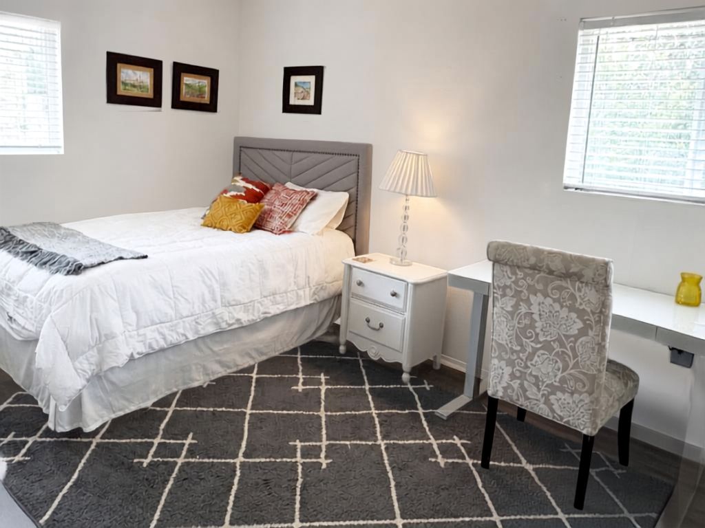 A bedroom with a bed, bedside table, chair, and a desk.