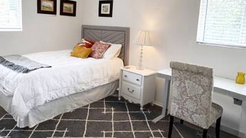A bedroom with a bed, bedside table, chair, and a desk.