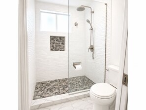 Eine Dusche mit barrierefreiem Einstieg, einer Glastür, einem kleinen Fenster und einer Toilette mit Marmorboden.