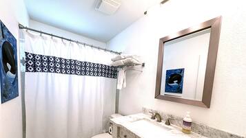 Ein Badezimmer mit Duschvorhang, Toilette, Waschbecken mit Seifenspender und Spiegel.