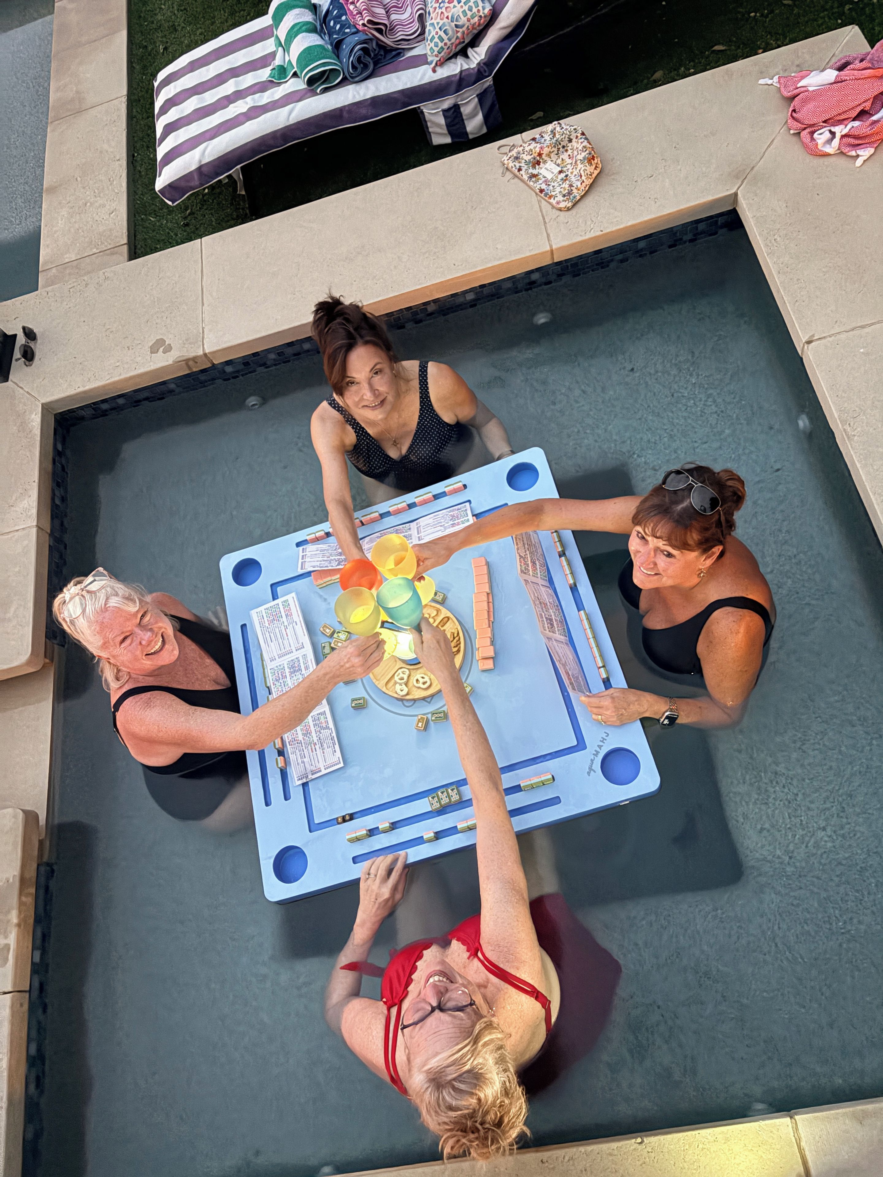 Een tafel bij het zwembad met een spel, omringd door vier personen.