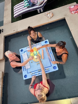 A poolside table with a board game, surrounded by four people.