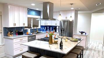A modern kitchen with white cabinets, a large island with bar stools, stainless steel appliances, and pendant lighting.