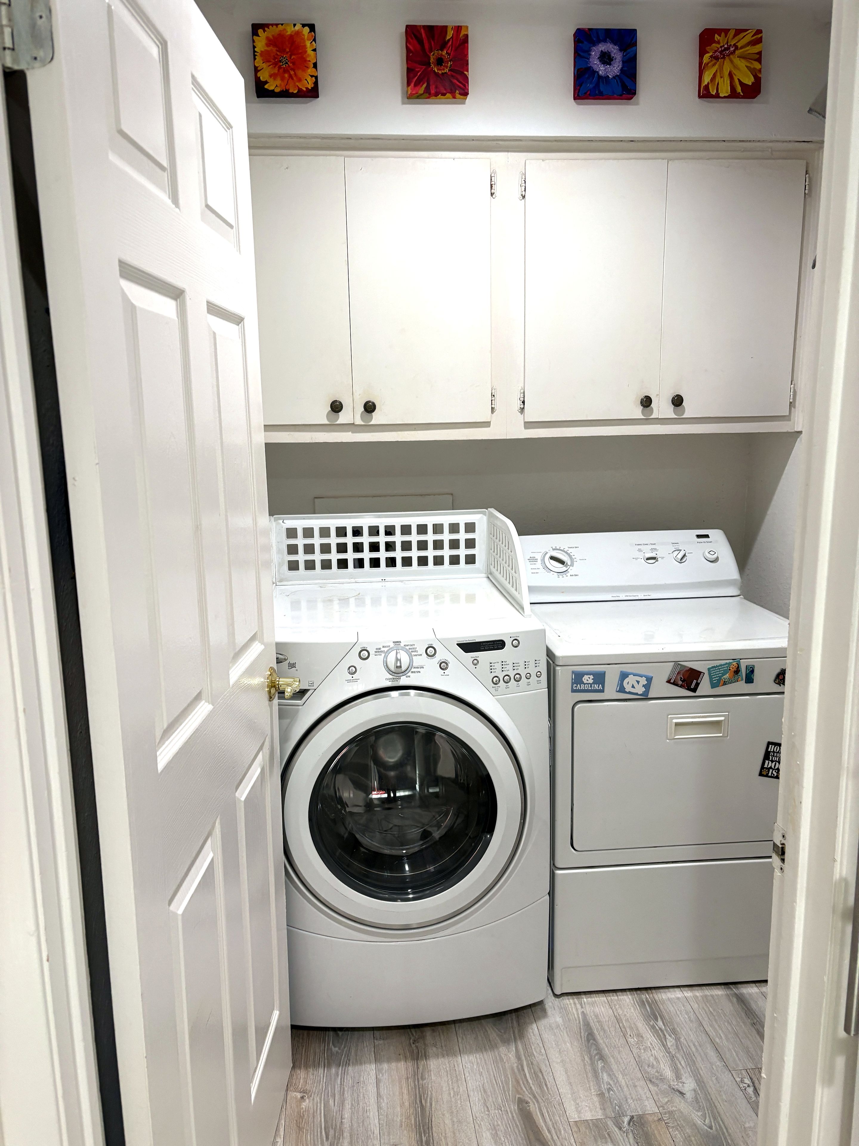 Een wasserette met een voorlader wasmachine en droger, witte kasten erboven en een deur aan de linkerkant.