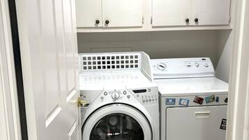 Een wasserette met een voorlader wasmachine en droger, witte kasten erboven en een deur aan de linkerkant.