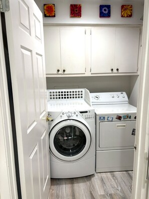 A laundry room with a front-loading washing machine and dryer, white cabinets above, and a door to the left.