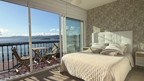 A bedroom with a large bed, a nightstand, and a chair. It has a balcony with a view of the sea and mountains. - Portosin, a beautiful home with spectacular views of the Muros-Noia estuary (Portosin)