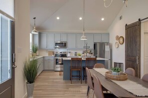 A modern kitchen with a central island, stainless steel appliances, and a dining area with wooden chairs and a table. - Freetown Farmhouse | Modern 3BR w/Big Kitchen (Lafayette)