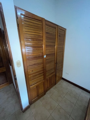 Un armario de madera con puerta corredera, suelo de baldosas y pared blanca.