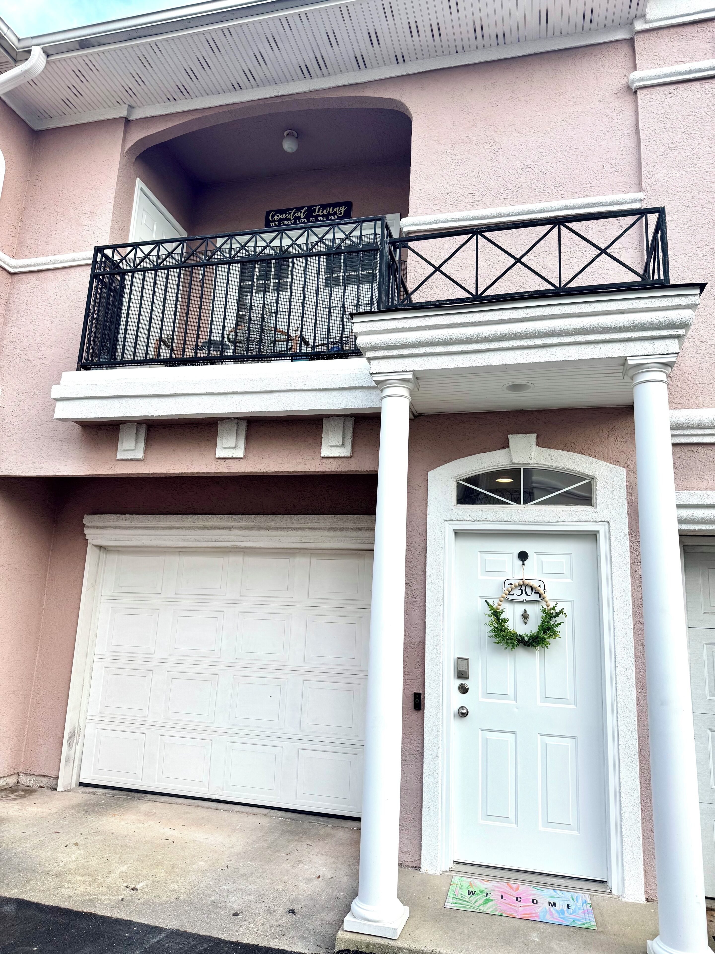 Une maison à deux étages avec un balcon, une porte de garage et une porte d’entrée ornée d’une guirlande.