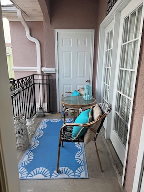 A balcony with a wicker chair, a small table, a blue patterned rug, and a white door. - Welcome to "The Coastal Beach Villa"- Your Seaside Retreat in Gulfport, MS! (Gulfport)