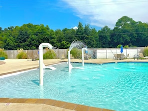 A swimming pool with a water feature, surrounded by a wooden deck and chairs. - Welcome to "The Coastal Beach Villa"- Your Seaside Retreat in Gulfport, MS! (Gulfport)