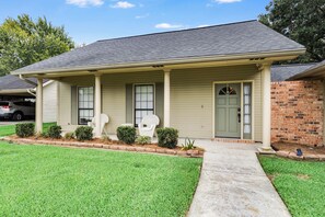 A single-story house with a front porch, a brick section on the right, and a green door.
