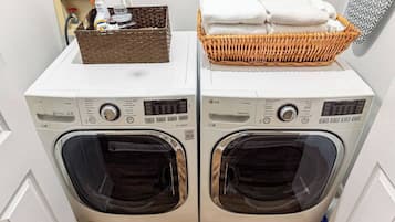 A laundry area with two front-loading washing machines, a basket with folded towels, and a cleaning spray bottle.