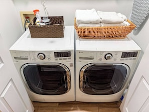 A laundry area with two front-loading washing machines, a basket with folded towels, and a cleaning spray bottle.