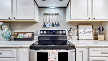 Una cocina con estufa, horno y utensilios colgando.