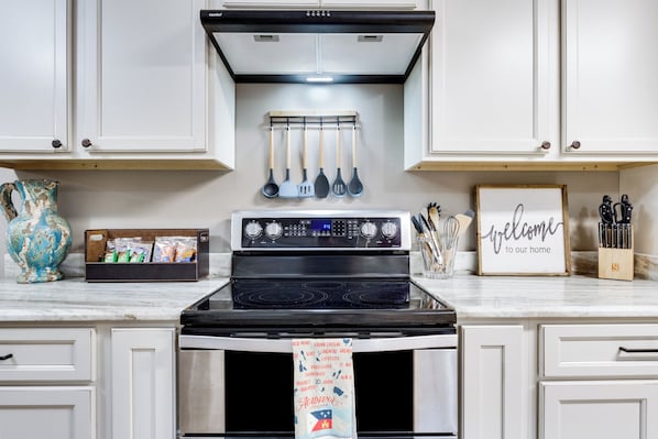 A kitchen with a stove, oven, and hanging utensils.