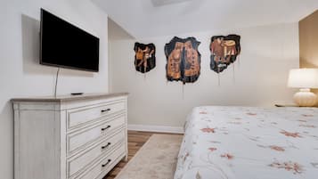 A bedroom with a TV mounted on the wall, a dresser, a bed with a floral bedspread, and wall-mounted artwork.