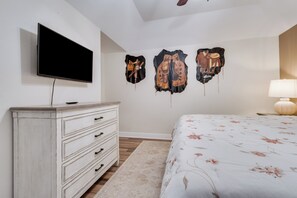 A bedroom with a TV mounted on the wall, a dresser, a bed with a floral bedspread, and wall-mounted artwork.