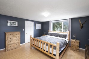 A bedroom with a wooden bed, a dresser, a nightstand, and a window with a view of trees.