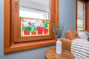 A room with a wooden-framed window, a white vase with green foliage, and a brown leather sofa.