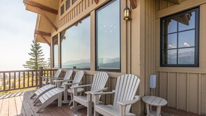 Terraza de madera con sillas Adirondack y una mesa, con vista a un paisaje montañoso.