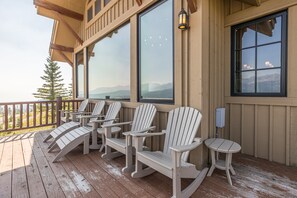 A wooden deck with Adirondack chairs and a table, overlooking a mountainous landscape. - NEW Listing | Ski In/Out + Private Hot Tub in Moonlight (Big Sky)