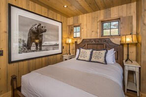 Un dormitorio con paneles de madera, una fotografía grande enmarcada, dos lámparas de noche y una cama con almohadones estampados.