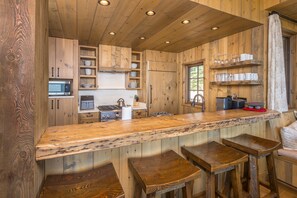 A wooden kitchen with a bar area, stools, and built-in appliances. - NEW Listing | Ski In/Out + Private Hot Tub in Moonlight (Big Sky)