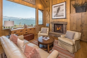A cozy living room with a fireplace, wooden furniture, and a view of mountains.