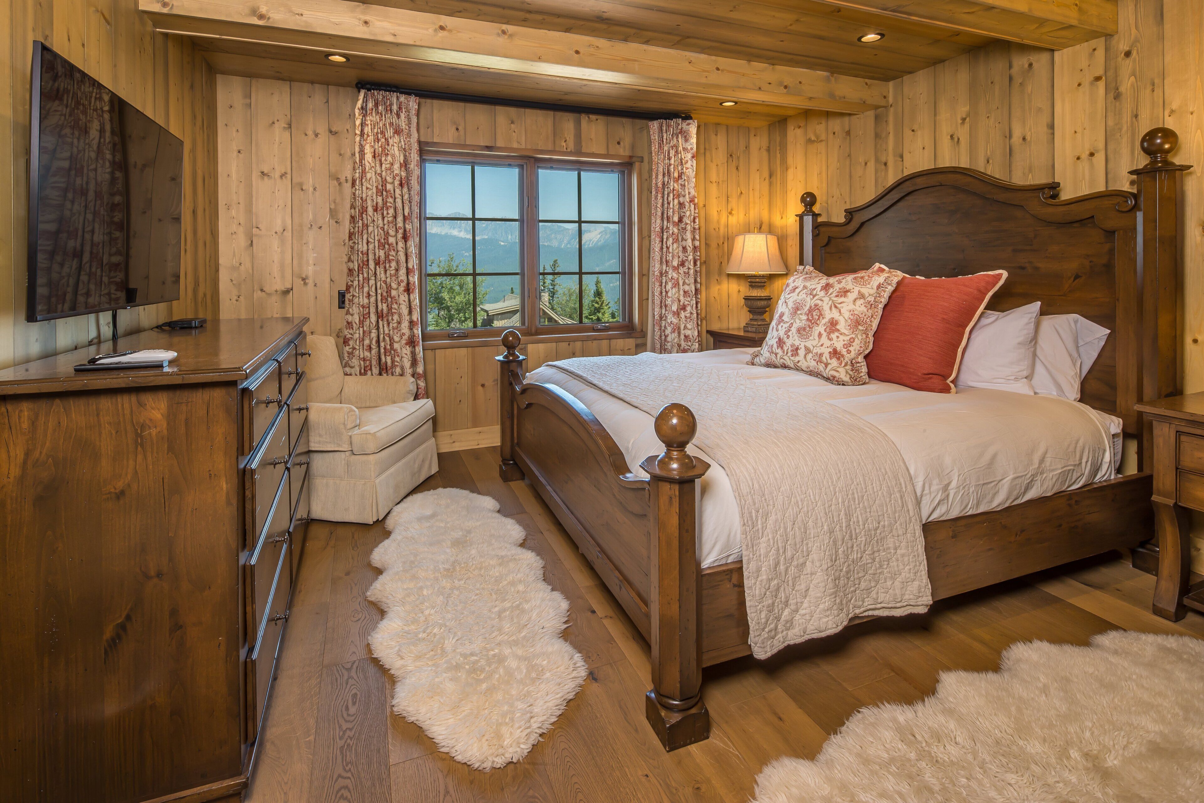 A wooden-paneled bedroom with a bed, a dresser, a television, and a window with a view.