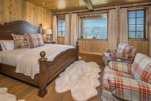Un dormitorio de madera con cama, sofá y vistas a la montaña, además de una alfombra mullida.