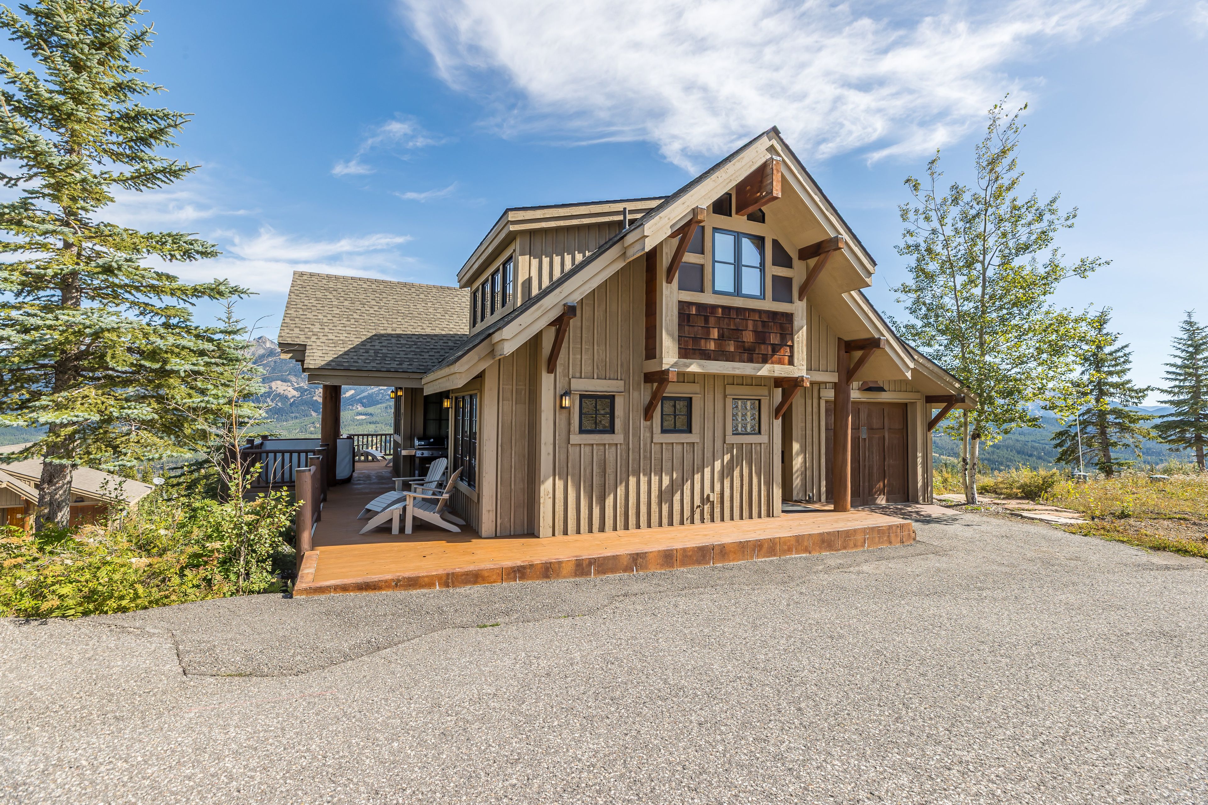 A wooden cabin with a deck, large windows, and a view of the mountains.