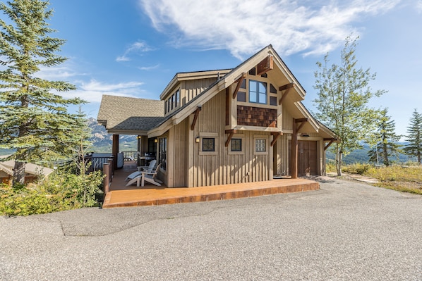 A wooden cabin with a deck, large windows, and a view of the mountains.