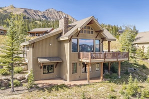 A two-story wooden cabin with a balcony, large windows, and a stone chimney.