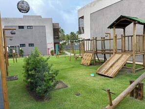 A playground with a slide, climbing structures, and a small tree.