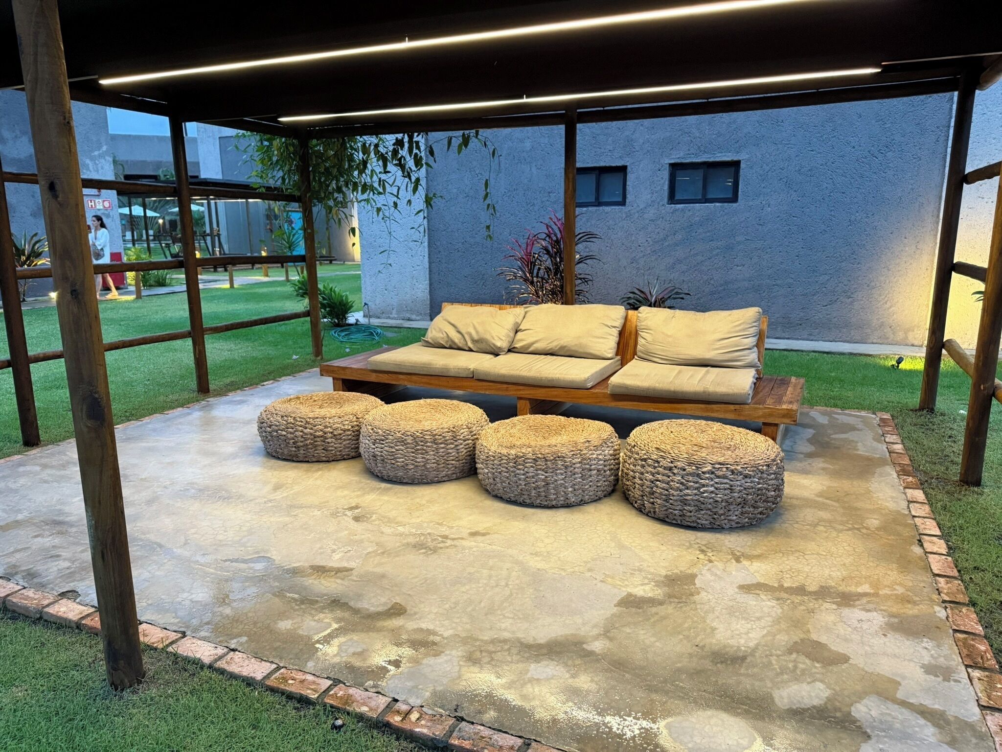 Un espace extérieur aménagé avec un canapé et des poufs, une pergola au-dessus et un sol en béton.