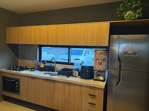 Una cocina moderna con gabinetes de madera, un refrigerador de acero inoxidable, un horno empotrado y un ventanal con vista a un estacionamiento.