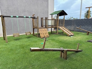 A wooden playground with swings, a slide, and climbing structures.